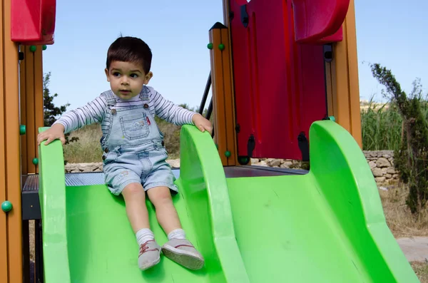 Lindo niño de dos años playig en el parque infantil al aire libre en el tobogán —  Fotos de Stock