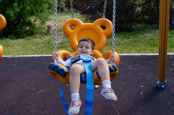 Lindo niño de dos años de edad playig en el parque infantil al aire libre en el columpio de oso de peluche —  Fotos de Stock