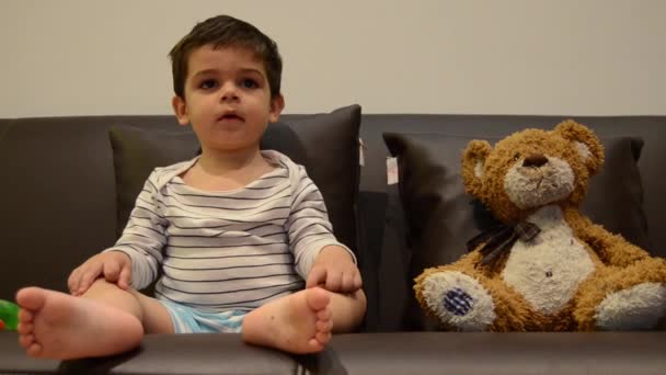 Niedliche zwei Jahre alte Junge vor dem Fernseher mit seinem Teddybär — Stockvideo