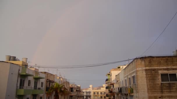 Buggiba, Malta 30. mei 2019 Rainbow ower residentiële gebouwen op donkere bewolkt regenachtig stormachtige dag — Stockvideo