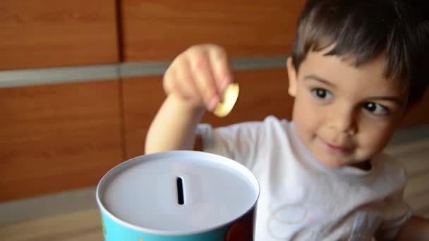 Симпатичная двухлетняя копила деньги, кладя монеты в металлический банк — стоковое видео