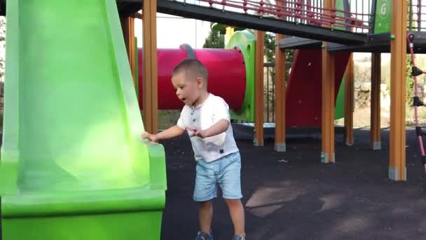 Очаровательный маленький мальчик играет на горке на детской площадке, замедленная съемка — стоковое видео