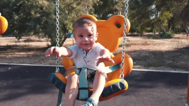 Schattige kleine jongen op een schommel met uitgestrekte handen in slow motion, met een grote glimlach op zijn gezicht — Stockvideo