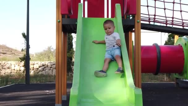 Menino adorável deslizando no slide no playground, câmera lenta — Vídeo de Stock