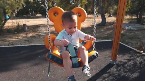 Schattige kleine jongen op een schommel met uitgestrekte handen in slow motion, met een grote glimlach op zijn gezicht — Stockvideo