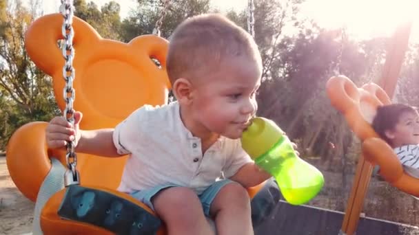 Children swinging on the swing in the park in slow motion — Stock Video