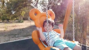 Sevimli çocuk, anaokulu öğrencisi yavaş çekimde boş bir parkta salıncakta sallanıyor.