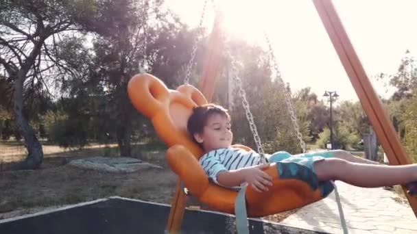 Чарівний хлопчик, дошкільник гойдається на гойдалках у порожньому парку в повільному русі — стокове відео