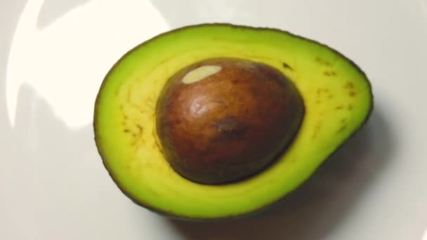 De helft van de avocado draait in slow motion op de witte plaat — Stockvideo