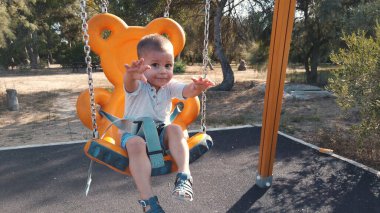 Yüzünde kocaman bir gülümsemeyle salıncakta sallanan sevimli küçük bir çocuk.