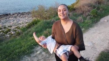Genç anne bebeğini döndürürken, büyük çocuk uzak bir yere taş atıyor. Sonbaharda deniz kıyısında