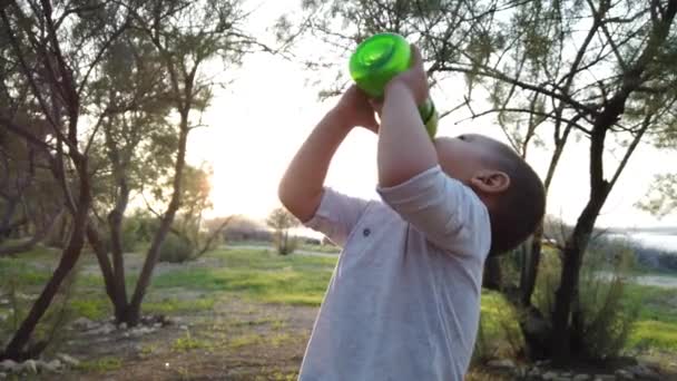 Adorable baby boy drinking water in the park during sunset — Stock Video