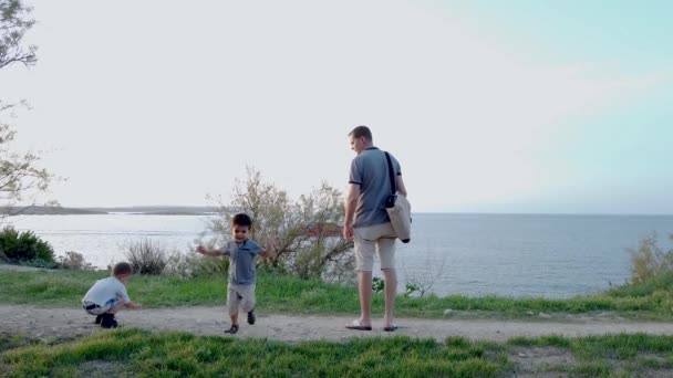 Familienzeit. Vater und Söhne an der Küste im herbstlichen Sonnenuntergang. Kleinkind rennt auf Kamera zu — Stockvideo