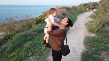 Genç anne bebeği kaldırıyor ve kucaklıyor. Sonbaharda deniz kıyısında