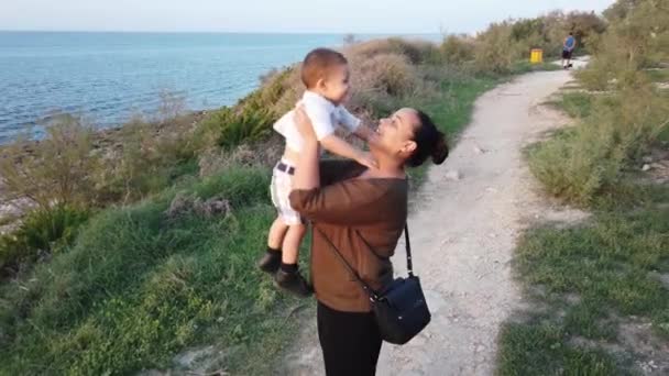 Jonge moeder tilt en knuffelt baby. Zeekust in de herfst — Stockvideo