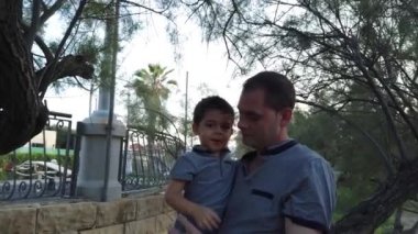 Baba oğul parkta oynuyorlar. Baba oğluna ağaçtan inmesini öğretiyor. Bebek ağaç kabuğuyla oynuyor.