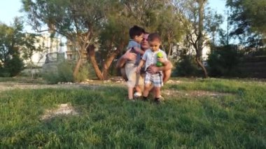 Baba parkta çömeliyor ve iki oğluna sarılıyor. Mutlu aile kavramı