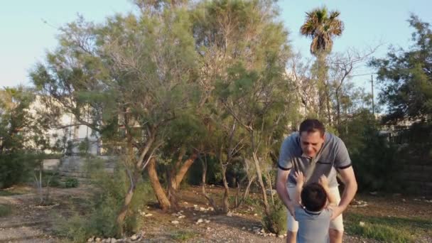 Gelukkige familie. Vader tilt zijn zoon op en draait hem rond in het park. Liefde en zorg — Stockvideo