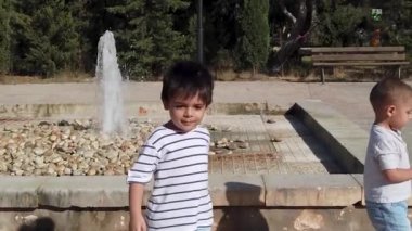 Sevimli çocuklar, güneşli bir günde çeşmenin yanında oynayan kardeşler.