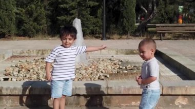 Sevimli çocuklar, güneşli bir günde çeşmenin yanında oynayan kardeşler.