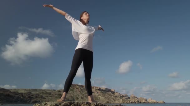 Концепція благополуччя. Молода біла жінка практикує йогу на скелястому пляжі — стокове відео