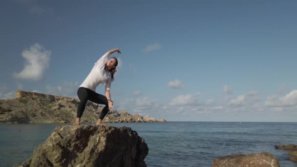 Young caucasian woman practising yoga on the rocky beach — Stock Video