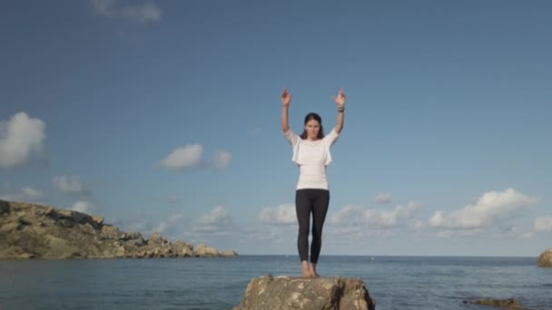 Mujer caucásica joven está haciendo yoga y ejercicios de estiramiento en la roca en la playa — Vídeo de stock