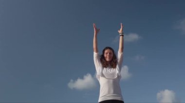 Mavi gökyüzüne karşı kaya üzerinde yoga yapan genç bir kadın.