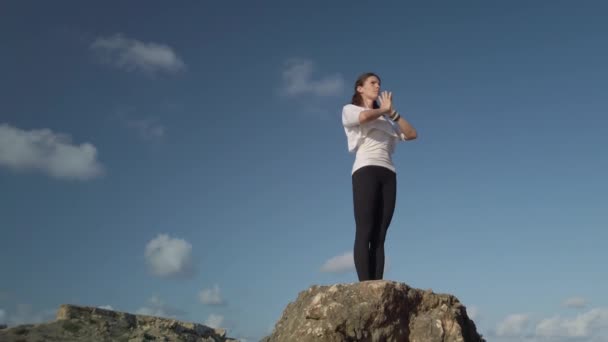 Молода біла жінка робить вправи для дихання йоги і розтягування на скелі на пляжі — стокове відео
