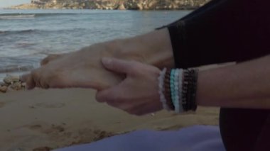 Yaklaş, genç kadın ayaklarını tutuyor ve sabahın erken saatlerinde kumlu sahilde yoga pozisyonunda kaldırıyor. Seçici odak açıcı atış