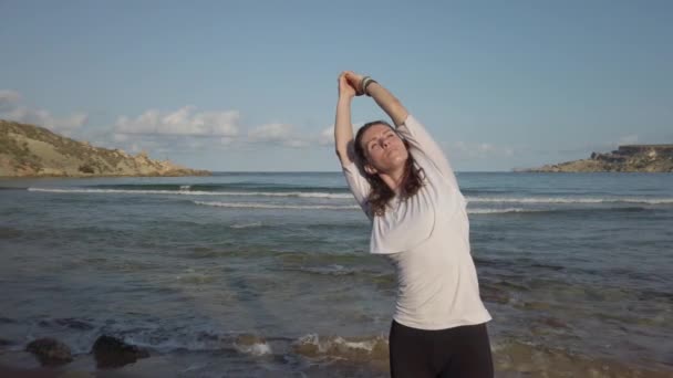 Młoda zmysłowa kobieta ćwicząca jogę na piaszczystej plaży w eraly rano złote światło słoneczne — Wideo stockowe