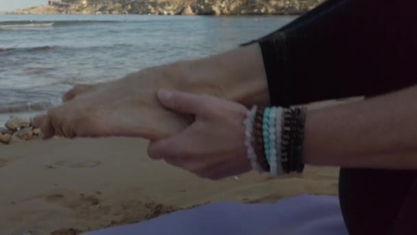 Zamknij się, młoda kobieto trzymająca stopy i podnosząca je w pozycji do jogi na piaszczystej plaży wczesnym rankiem. Selektywne skupienie odsłaniające strzał — Wideo stockowe