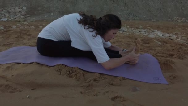 40 'lı yaşlarda bir kadın sabahın erken saatlerinde kumlu sahilde yoga yapıyor. — Stok video