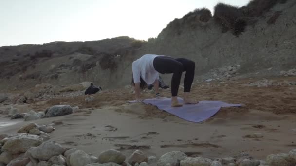 Женщина за 40 практикует йогу на песчаном пляже рано утром — стоковое видео