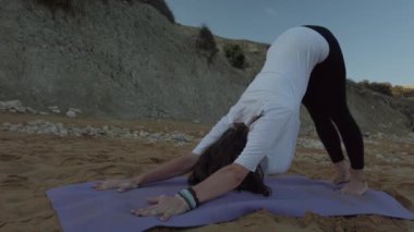 40 'lı yaşlarda bir kadın sabahın erken saatlerinde kumlu sahilde yoga yapıyor.
