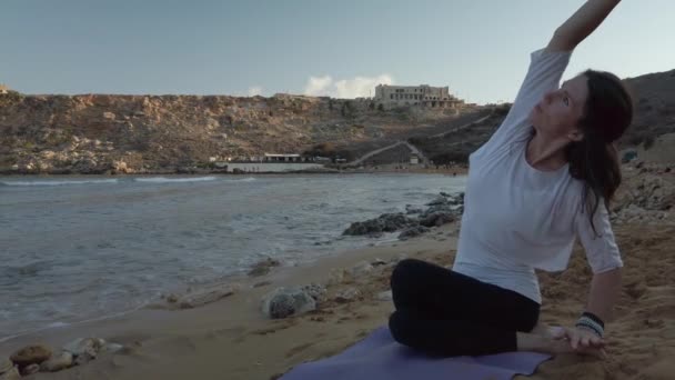 Kvinna på 40-talet tränar yoga på sandstranden tidigt på morgonen — Stockvideo