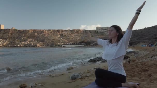 Kvinna på 40-talet tränar yoga på sandstranden tidigt på morgonen — Stockvideo