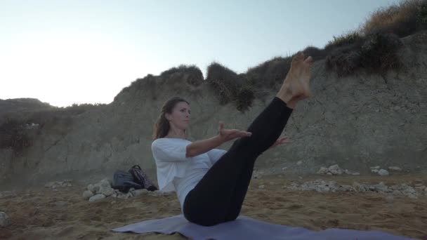 Vrouw in de 40 oefent yoga op het zandstrand in de vroege ochtend — Stockvideo