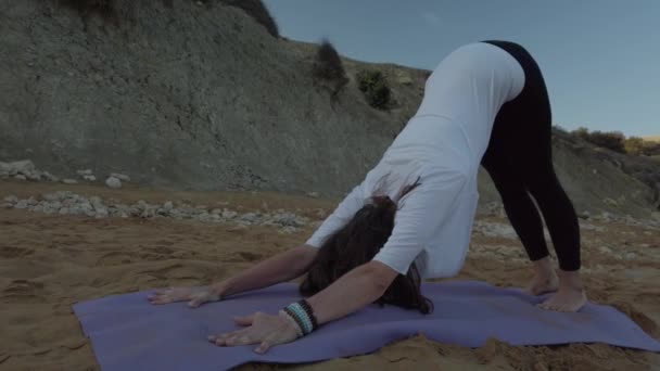 Kobieta po 40-tce ćwiczy jogę na piaszczystej plaży wczesnym rankiem — Wideo stockowe