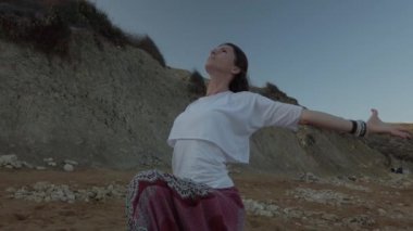 Genç beyaz bir kadın, kumral, sonbahar sabahının erken saatlerinde kumsalda yoga yapıyor.