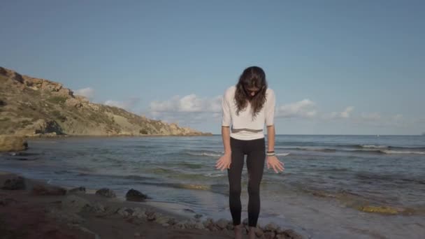 Giovane donna caucasica rimuovere la sabbia dai leggins sulla spiaggia di sabbia in prima mattina — Video Stock