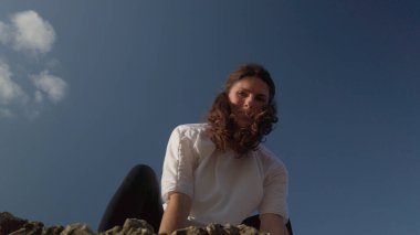 Mavi gökyüzüne karşı yoga yapan beyaz tenli bir kadın.