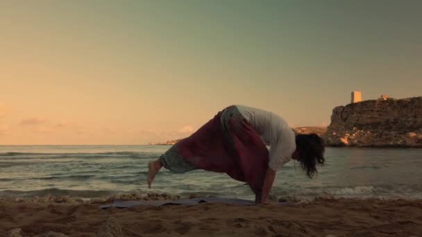 Kobieta po 40-tce ćwiczy jogę na piaszczystej plaży wczesnym rankiem. — Wideo stockowe