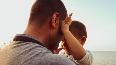 Genç beyaz bir baba oğlunu kucağında tutuyor. Bebek babasının yüzüne dokunuyor.