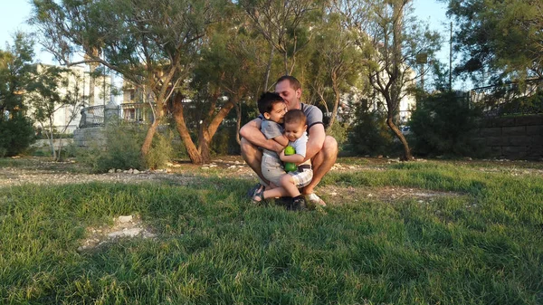 Padre joven abrazando a sus hijos en el parque. Concepto de familia feliz — Foto de Stock