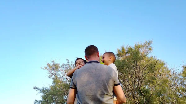 Padre joven abrazando a sus hijos en el parque. Concepto de familia feliz — Foto de Stock