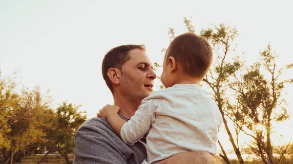 Joven padre caucásico sosteniendo a su hijo pequeño. Bebé tocando la cara de su padre —  Fotos de Stock