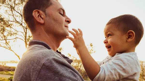 Joven padre caucásico sosteniendo a su hijo pequeño. Bebé tocando la cara de su padre —  Fotos de Stock