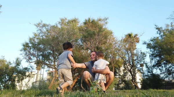 Padre joven abrazando a sus hijos en el parque. Concepto de familia feliz —  Fotos de Stock