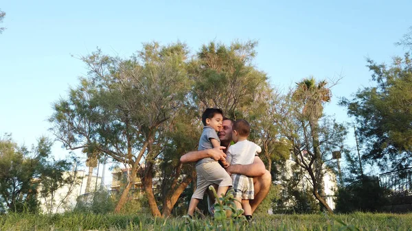 Padre joven abrazando a sus hijos en el parque. Concepto de familia feliz —  Fotos de Stock